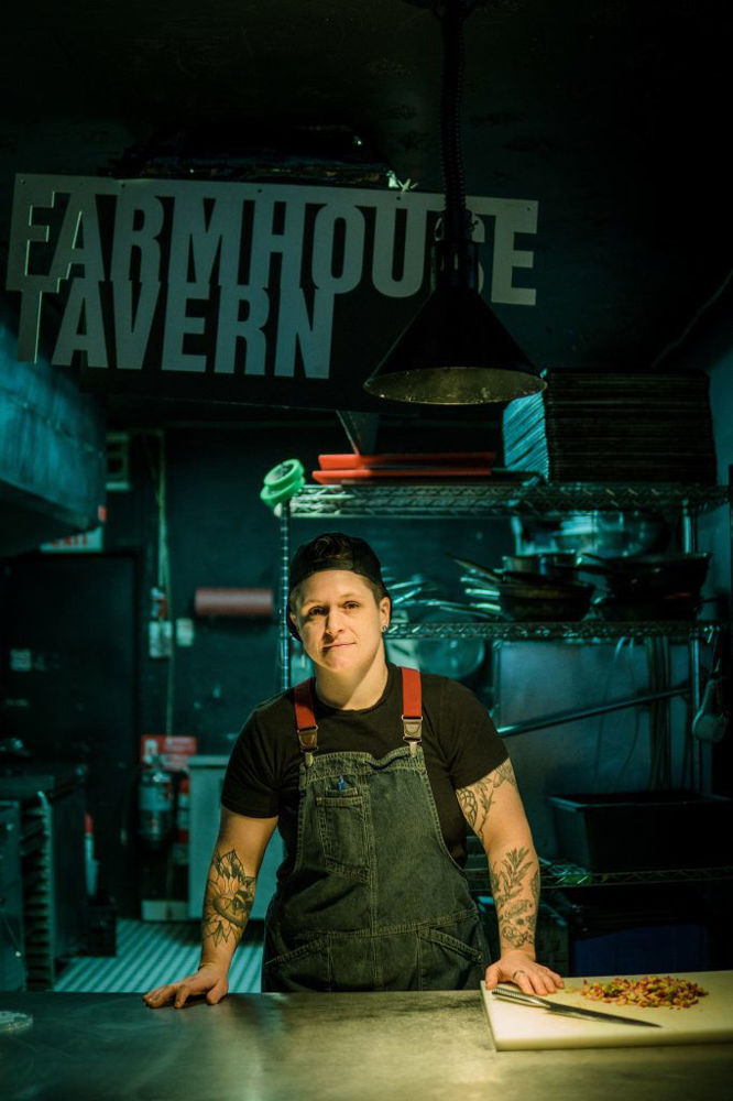Chef with tattoos standing in dark kitchen, sign for farmhouse tavern