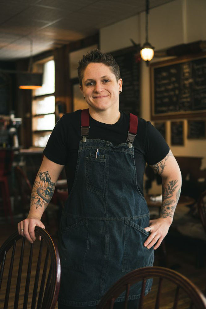 chef with tattoos smiling and standing in a warmly lit restaurant